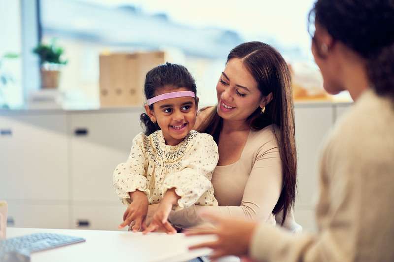 Ein junges Mädchen mit einem SoundBand in Lavendel sitzt auf dem Schoß seiner Mutter.