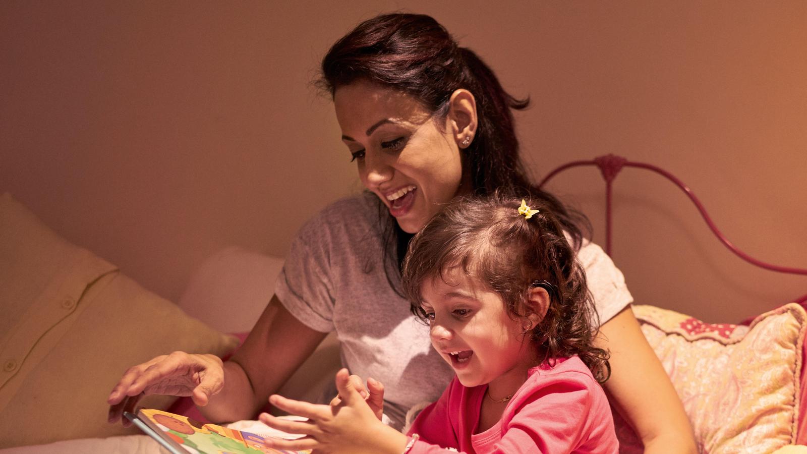 Un enfant portant un implant écoute sa mère lui lire un livre