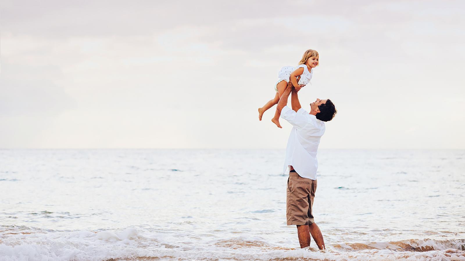 A man lifts up a young girl on the beach