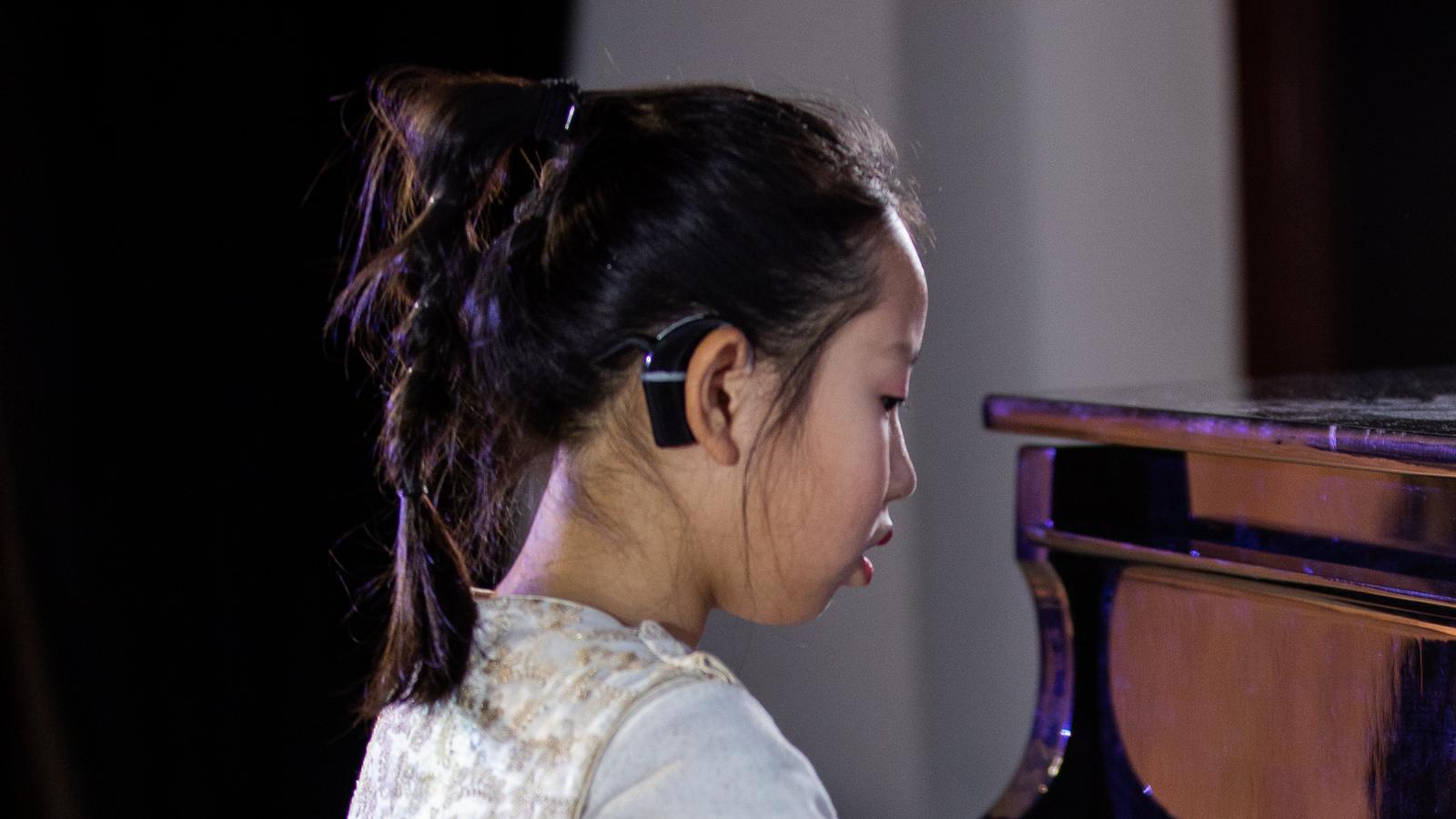 Một bé gái đeo thiết bị cấy bên trong đang chơi piano
