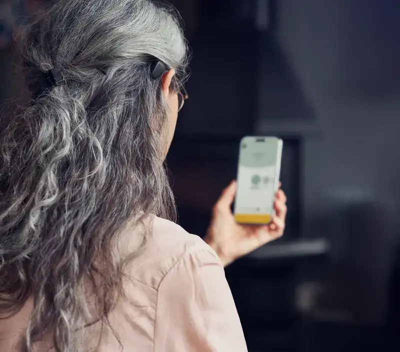 Femme portant un processeur Baha 7 et consultant l’application Baha Smart sur son téléphone.