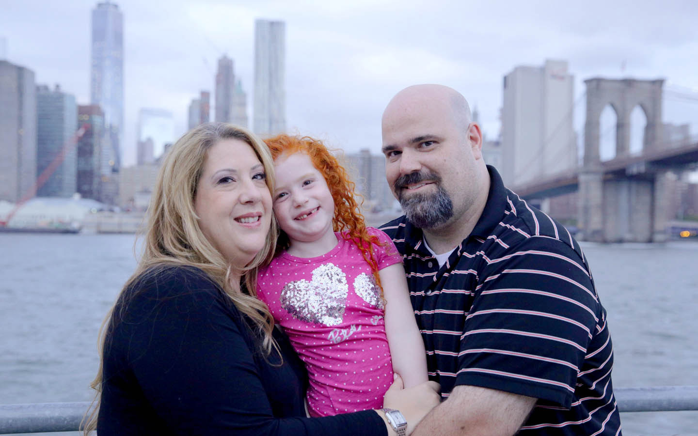Una familia con un implante auditivo y un miembro del programa Cochlear Family posan juntos. 