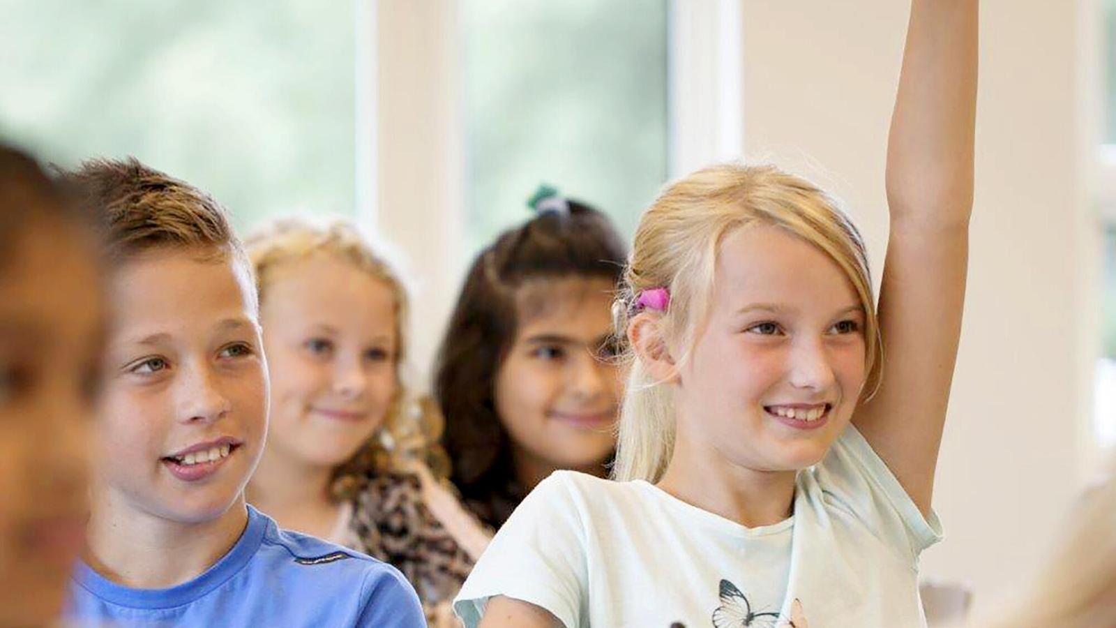 A girl wearing a Baha SoundArc raises her hand in class