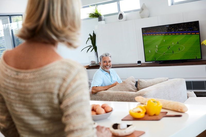 Bărbat adult urmărind un meci de fotbal la TV cu Cochlear Wireless TV Streamer (streamer TV)