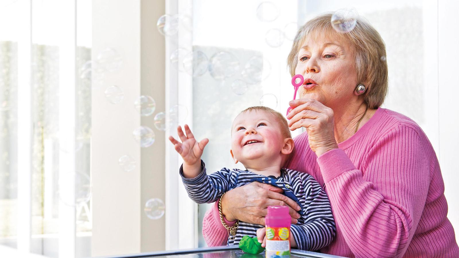 A woman blows bubbles as she holds her grandbaby