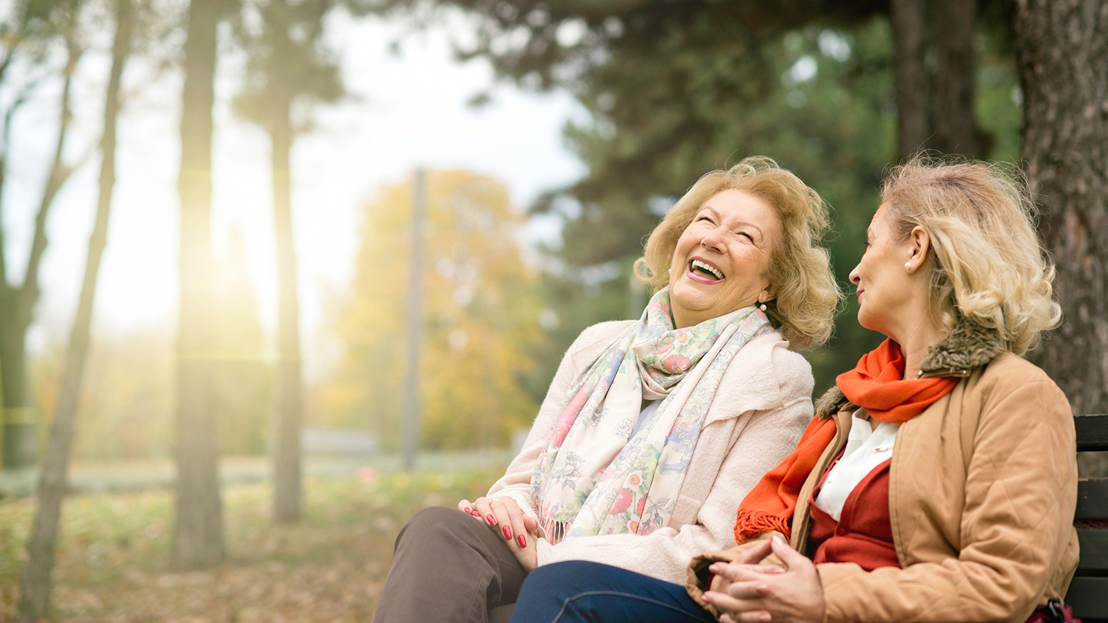 Zwei Frauen lachend in einem Park sitzend