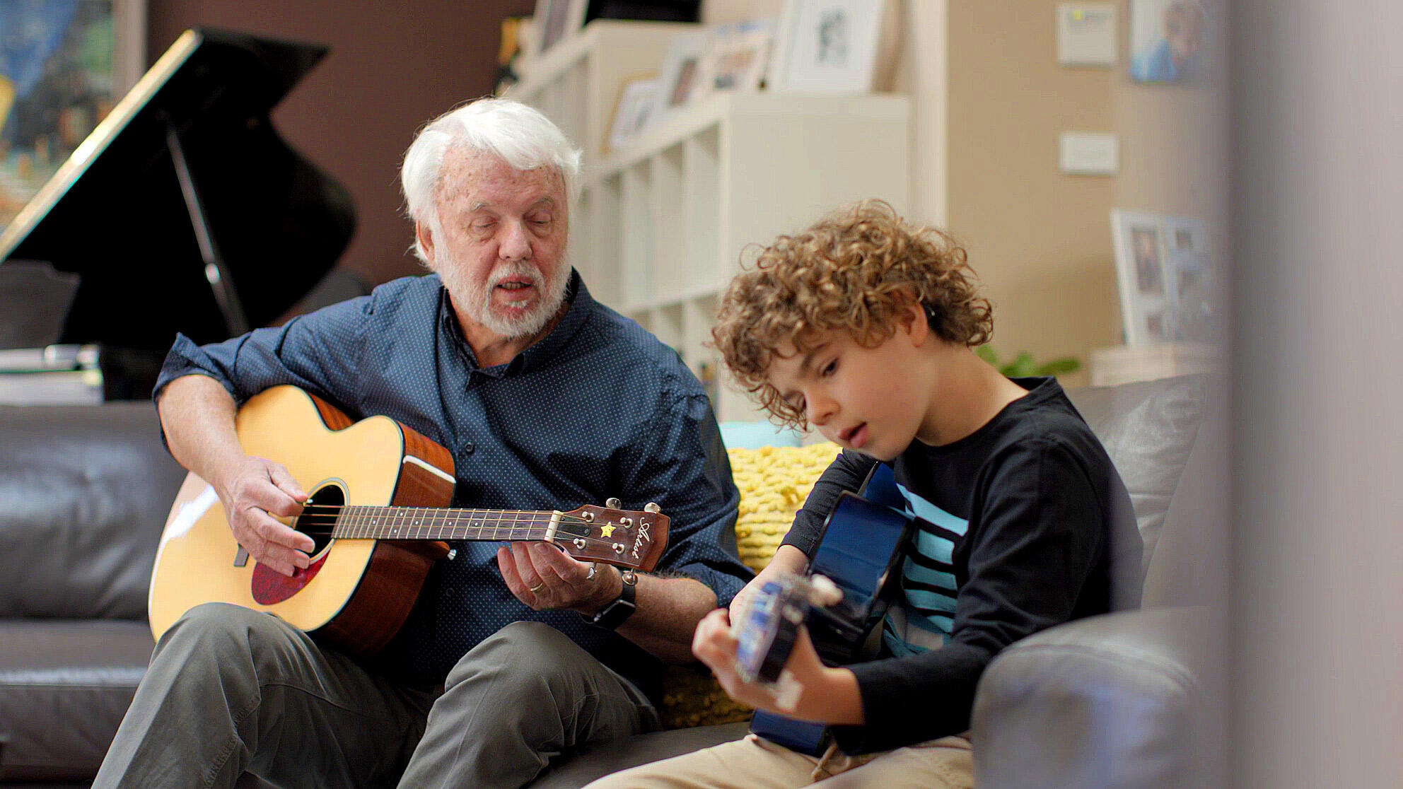 A man and a child wearing a Cochlear implant play acoustic guitars