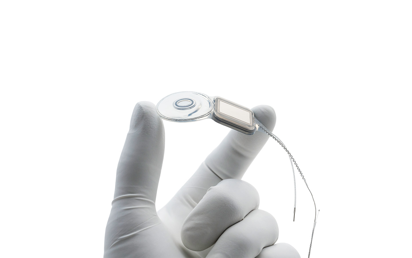 A surgeon's hand wearing a latex glove holds a Nucleus implant