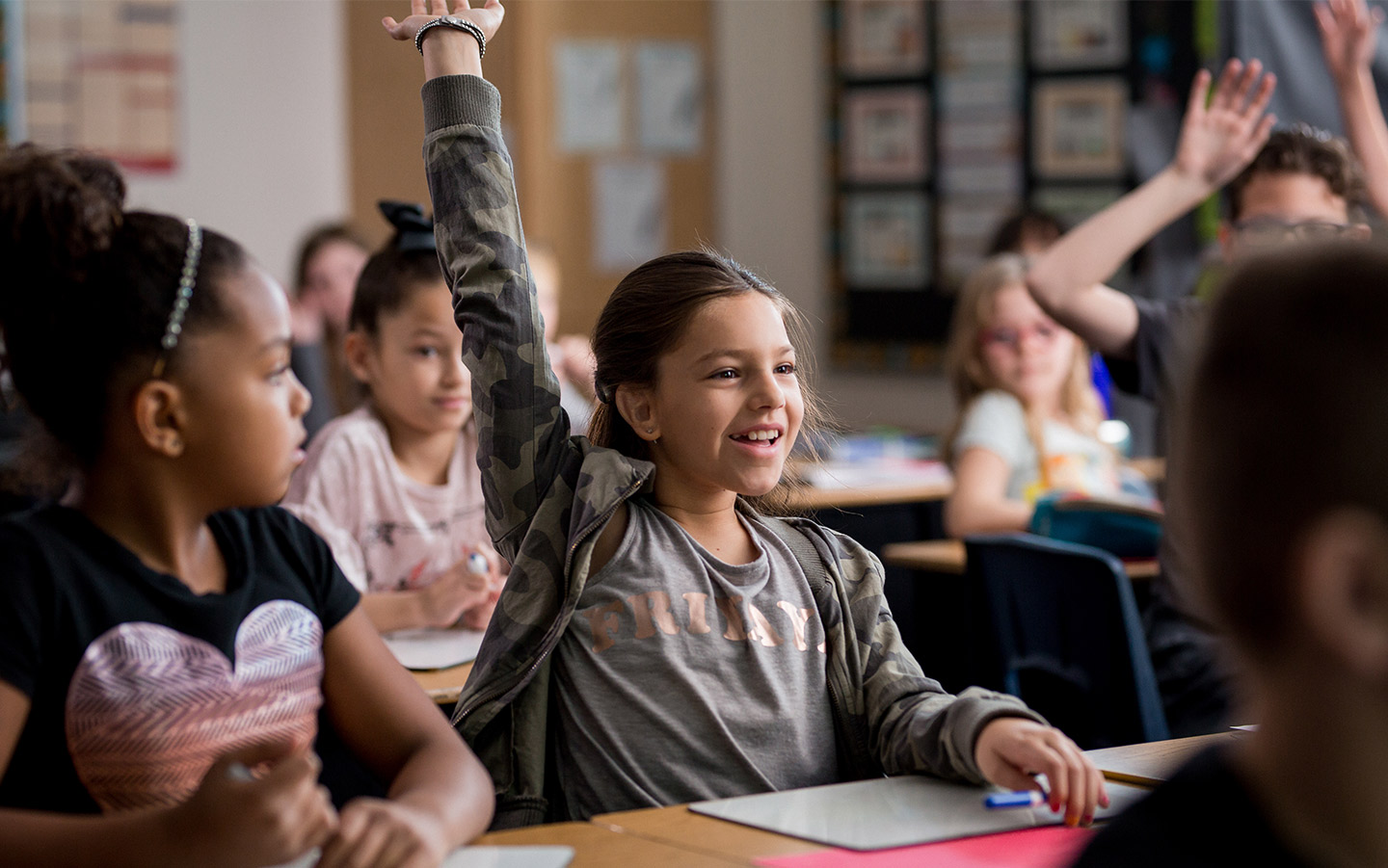 A girl wearing a Cochlear implant raises her hand in the classroom
