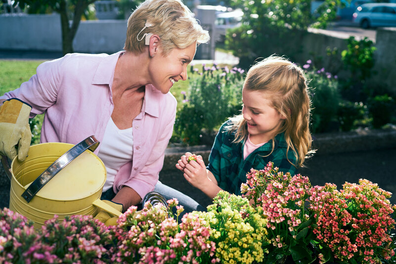 A woman waters flowers and a young girl is with her