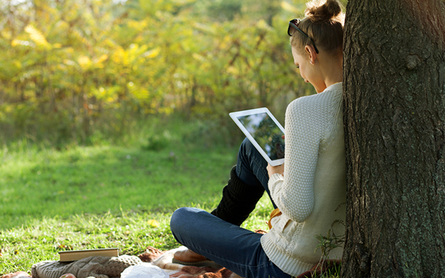 Seorang wanita sedang membaca dari iPad di sebuah taman