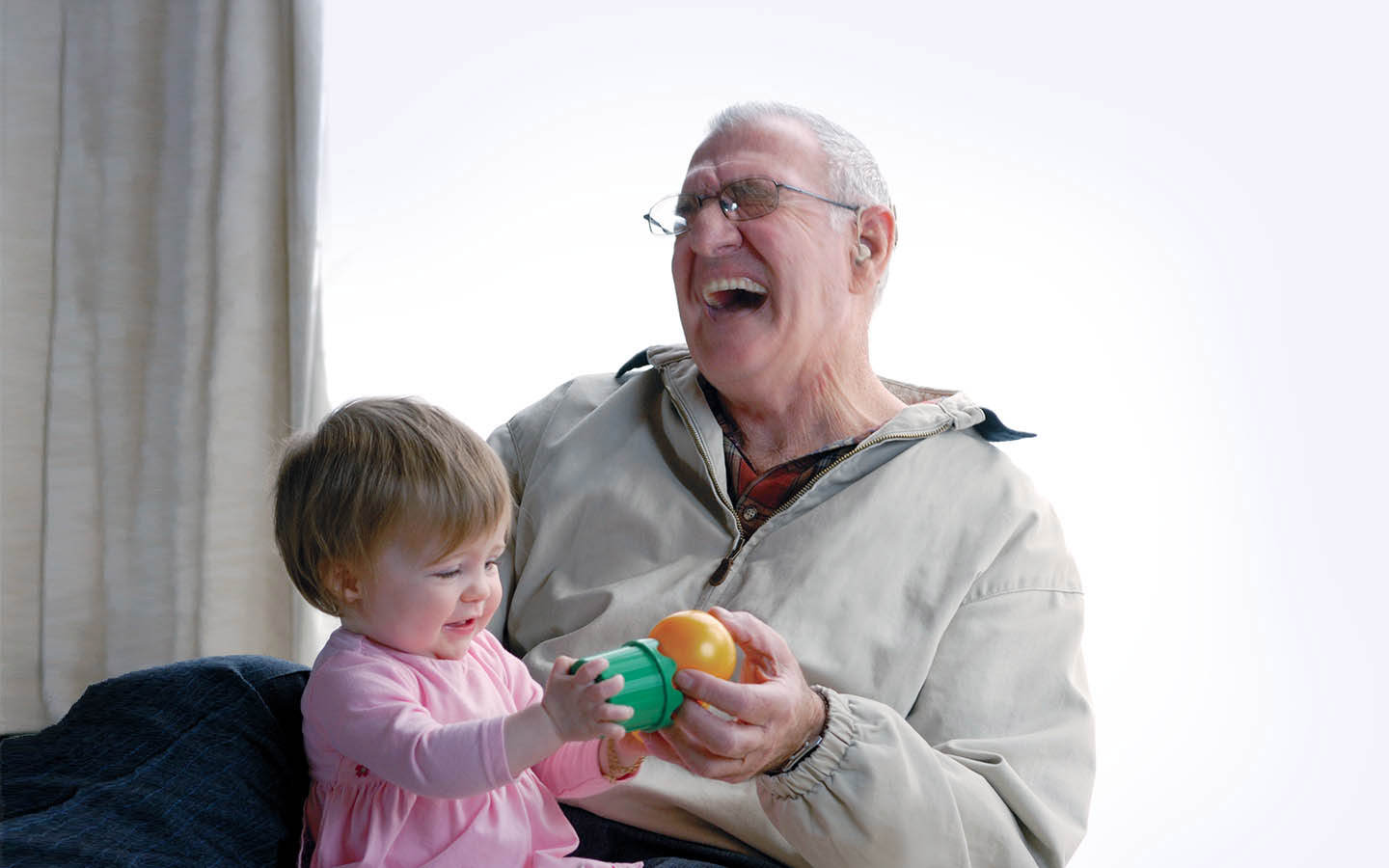 ผู้รับการผ่าตัดฝังประสาทหูเทียมที่เป็นคนสูงวัยกำลังหัวเราะโดยมีหลานชายนั่งอยู่บนตักของเขา