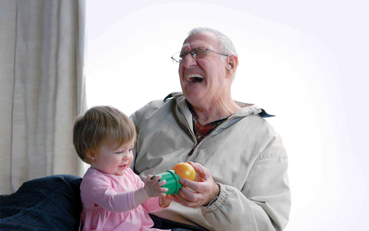 Grandfather laughs as his grandaughter sits on his lap