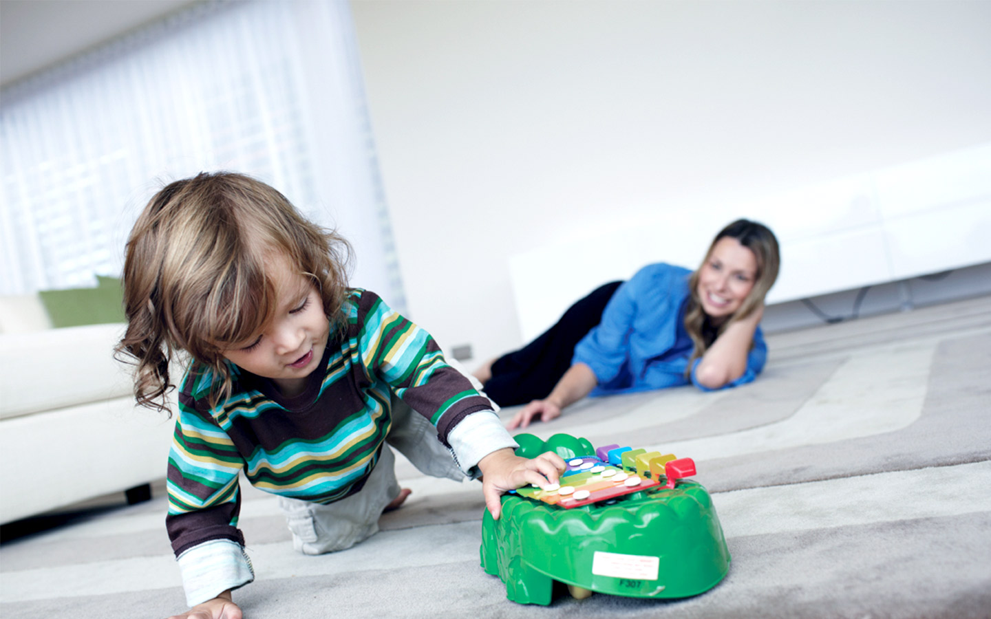 A young boy plays with a xylophone as a woman watches on