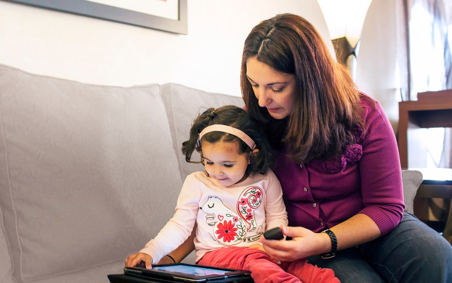 A woman reads with her young daughter on an iPad