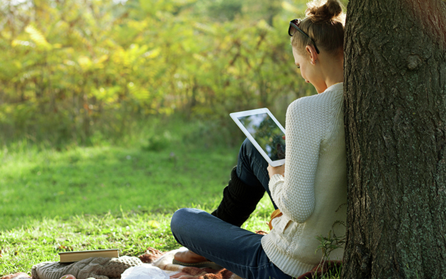A woman sits in a park with an iPad