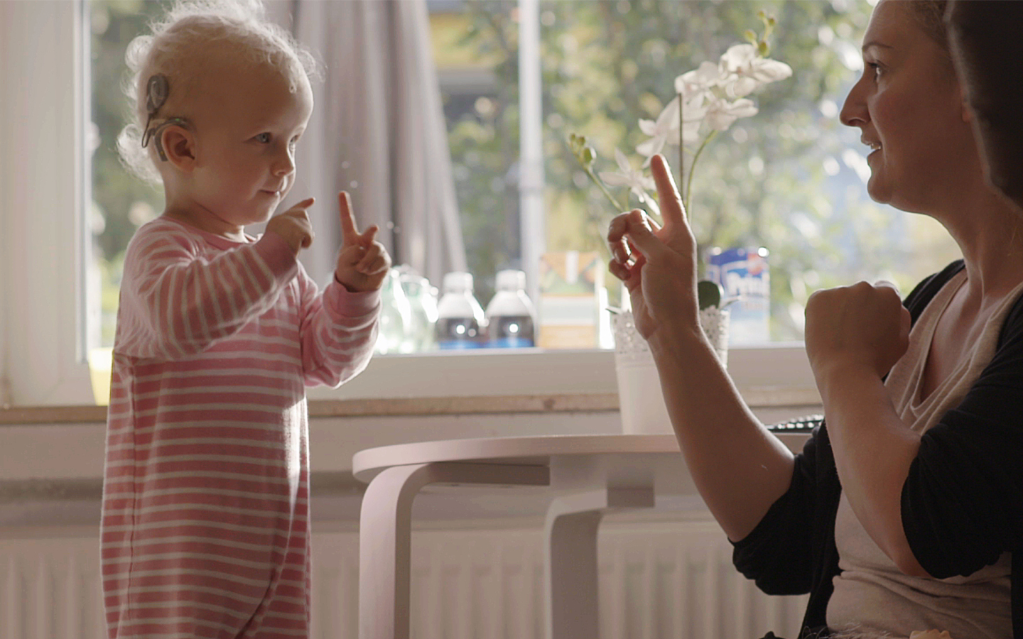 Egy cochleáris implantátumot viselő kisgyermekkel kommunikáló hölgy 
