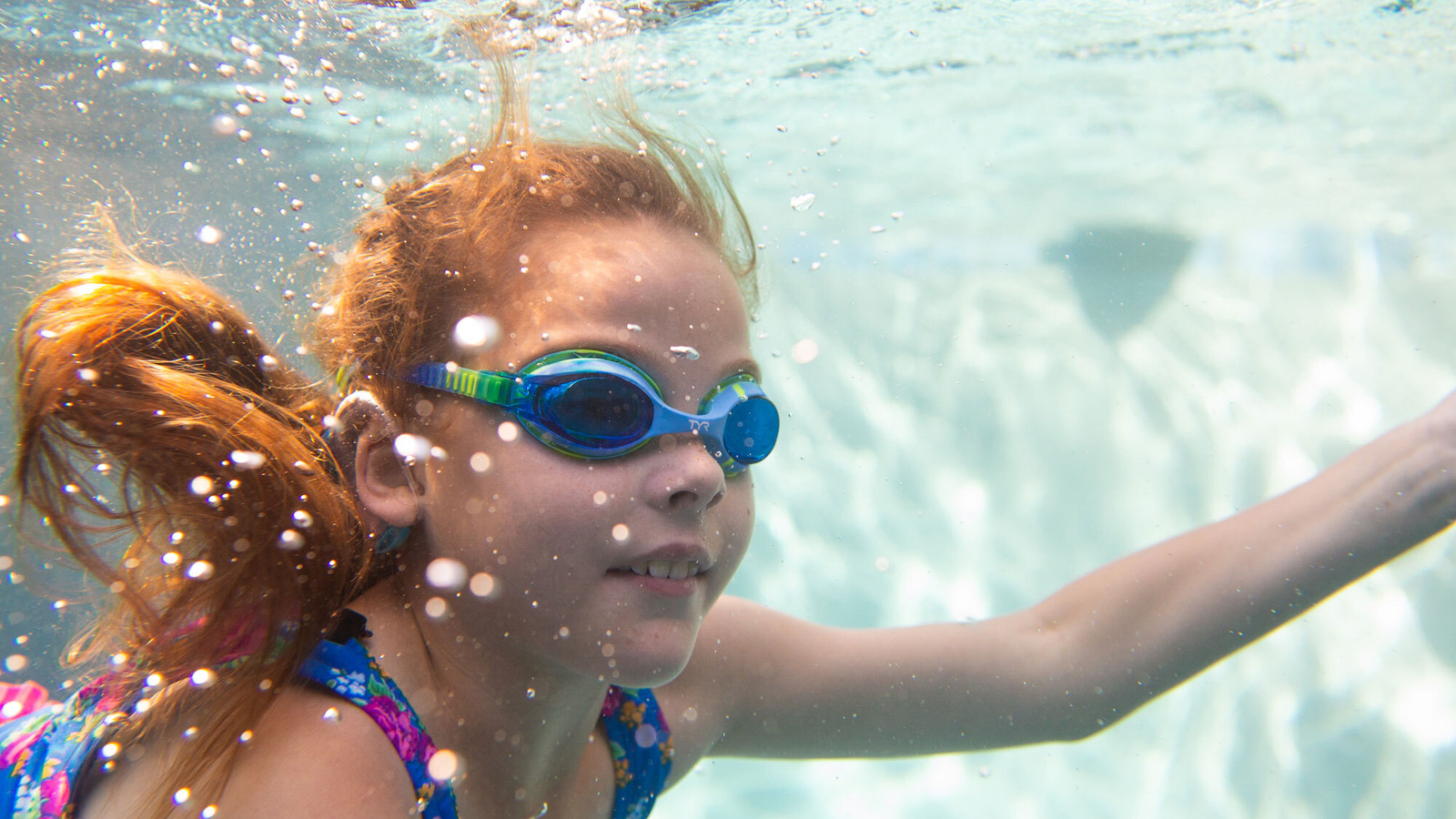 Red haired girl in a blue swimming suit is diving in a swimming pool