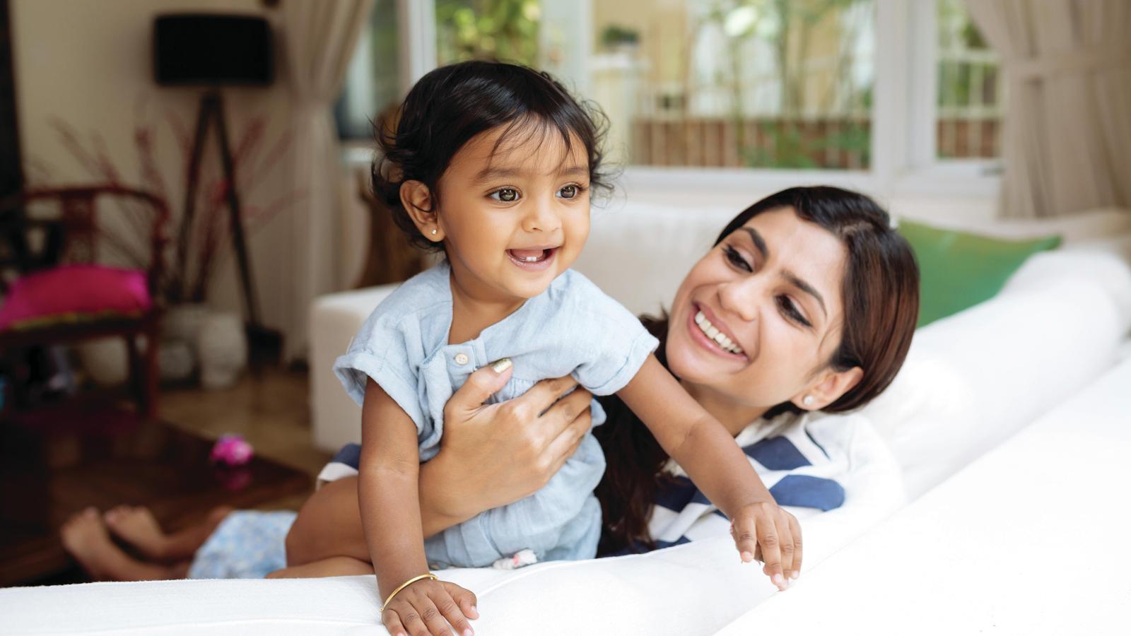 A woman smiles at her toddler as they sit on the couch