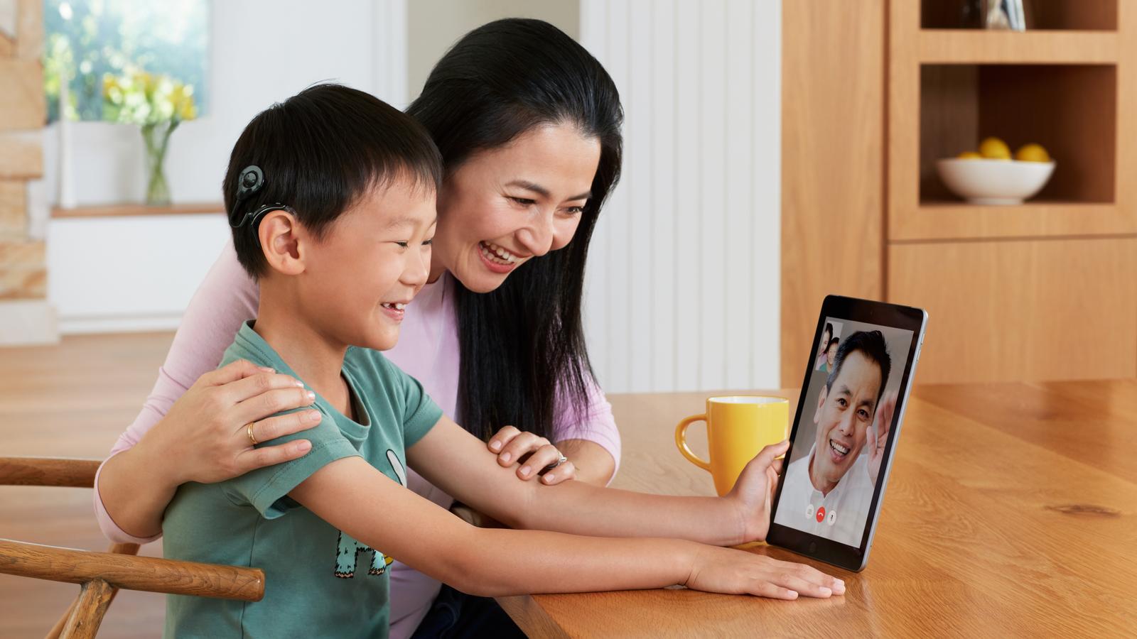 Rapaz asiático com o processador de som Nucleus conversando com seu pai via Facetime