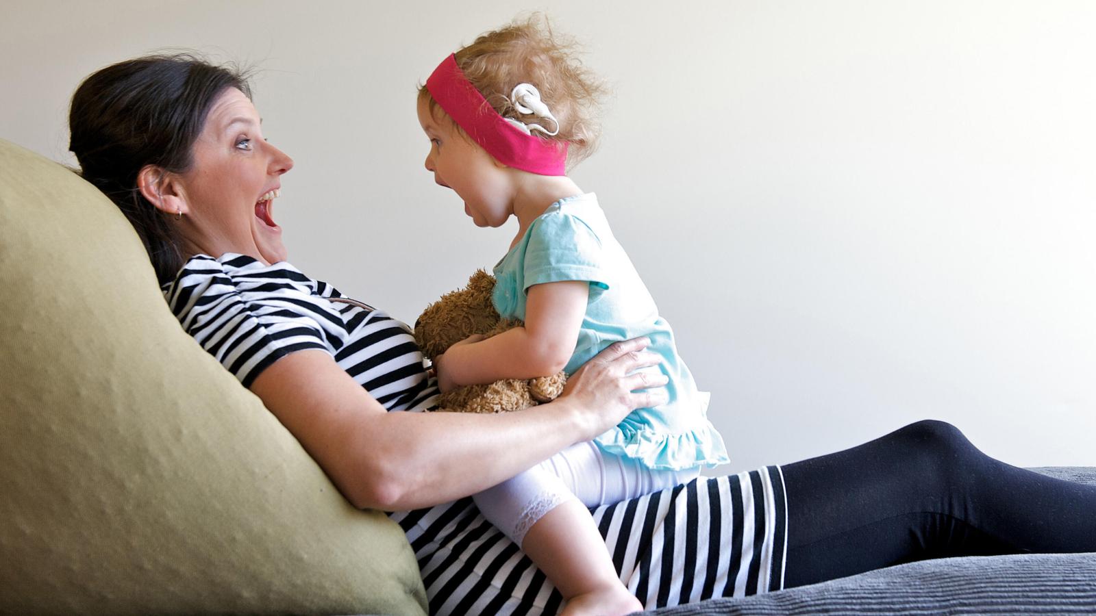 Uma criança com implante ri sentada no colo da mãe