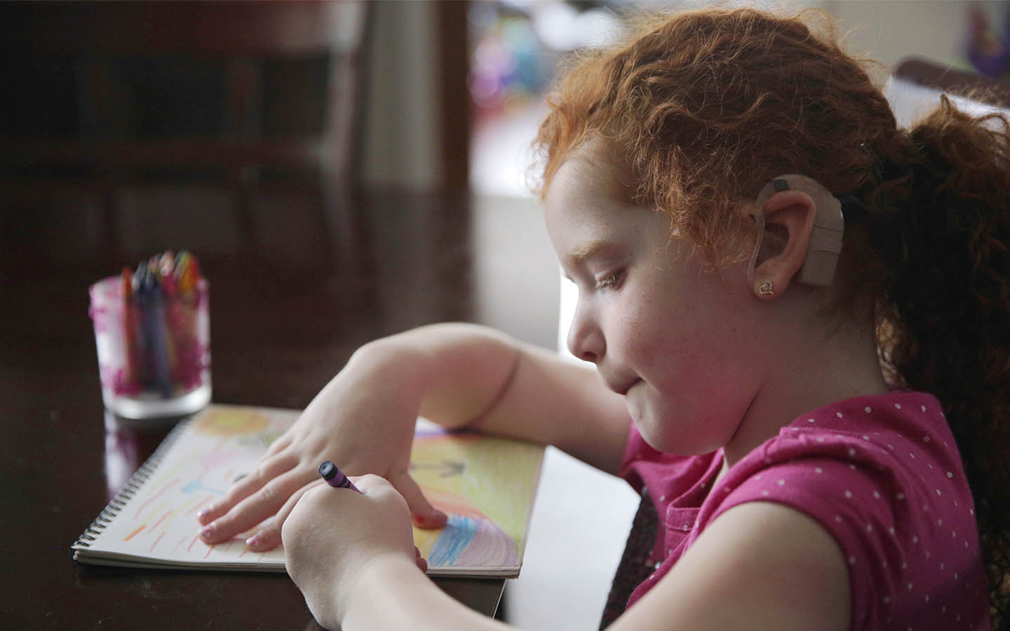 A young girl with a Cochlear implant draws with crayons