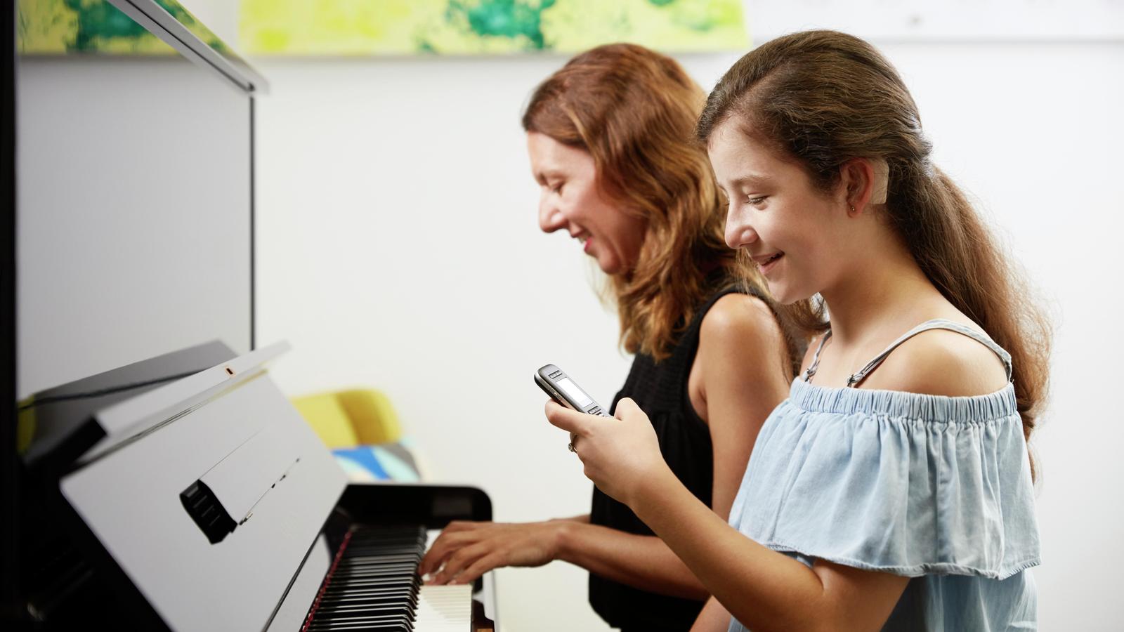 Teeanage girl uses microphone while her mother plays the piano