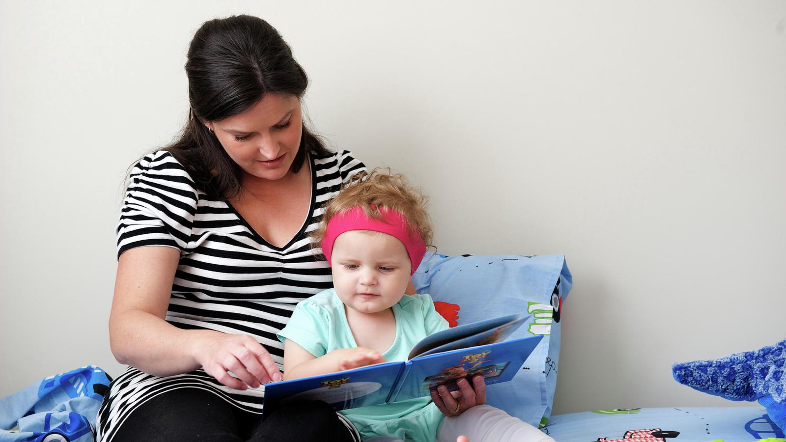 一位女性為配戴聽力裝置的孩子讀書