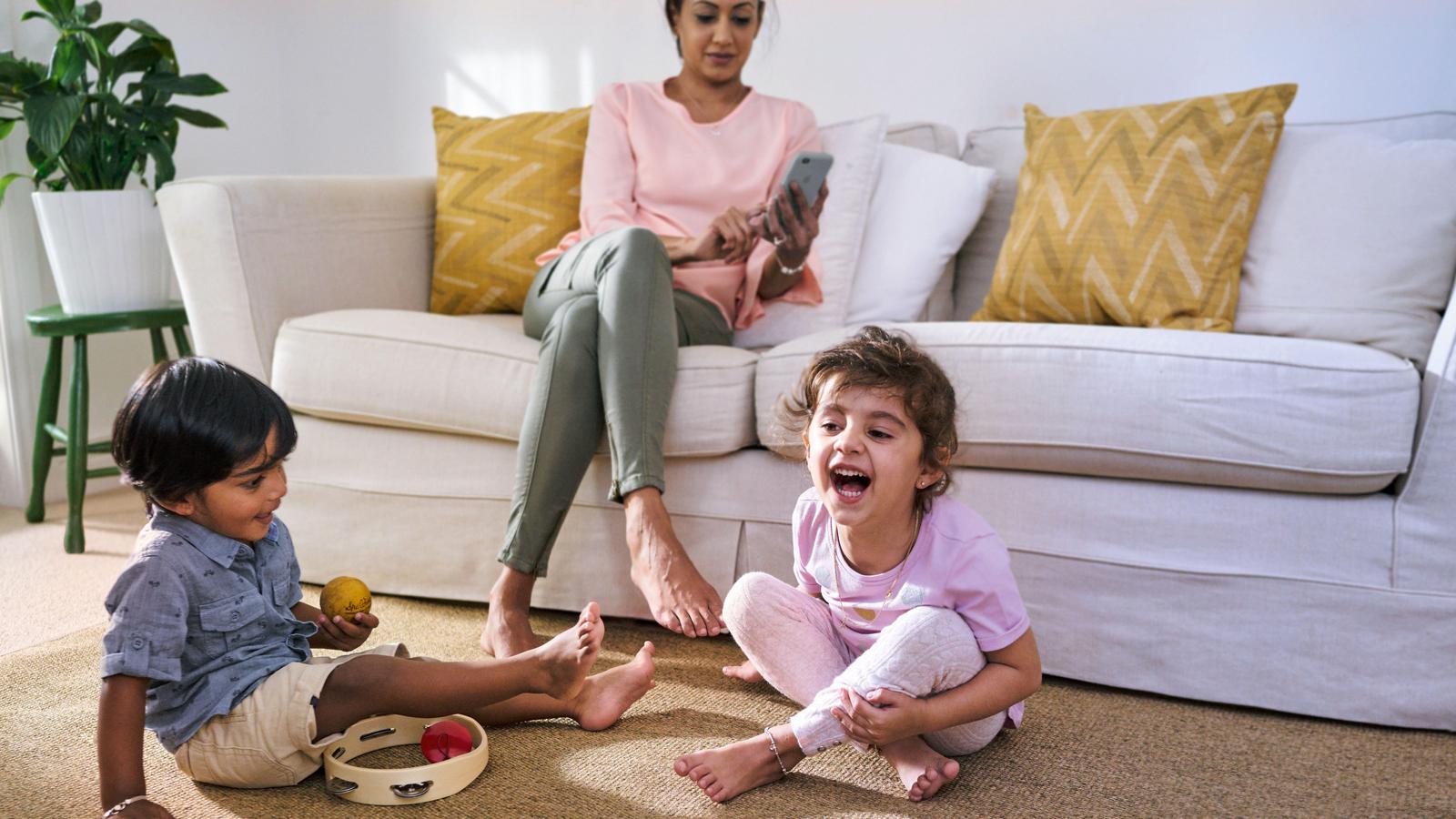 Two children playing in lounge room as their mother watches on