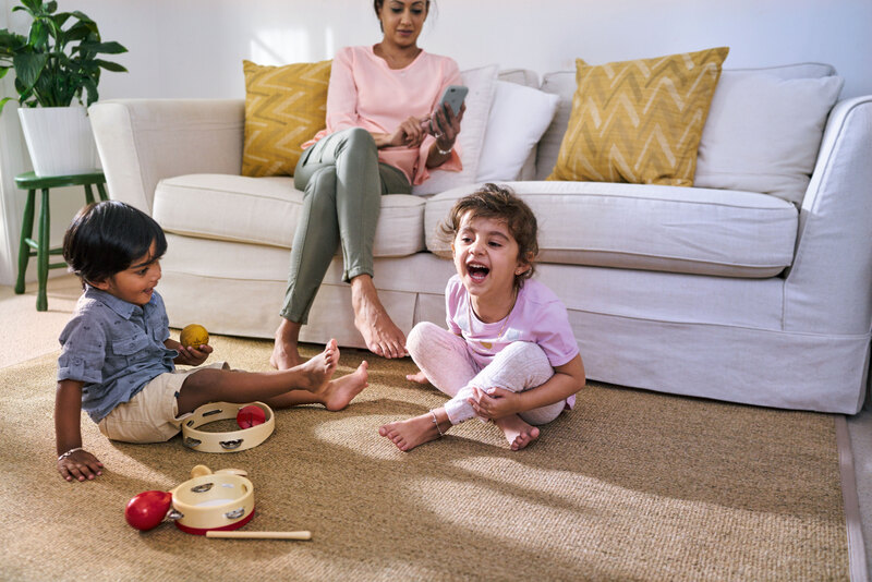 Dos niños jugando en una sala mientras su madre los mira