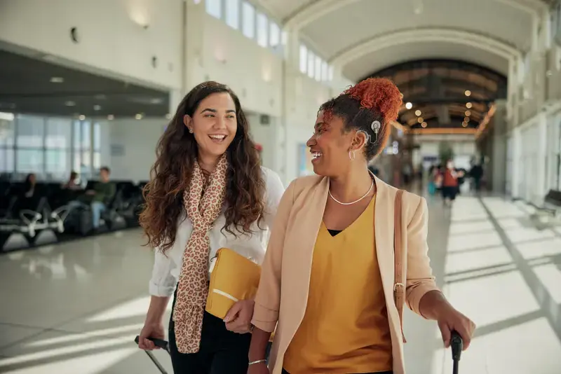 Woman wearing a cochlear implant walking through an airport with a friend.