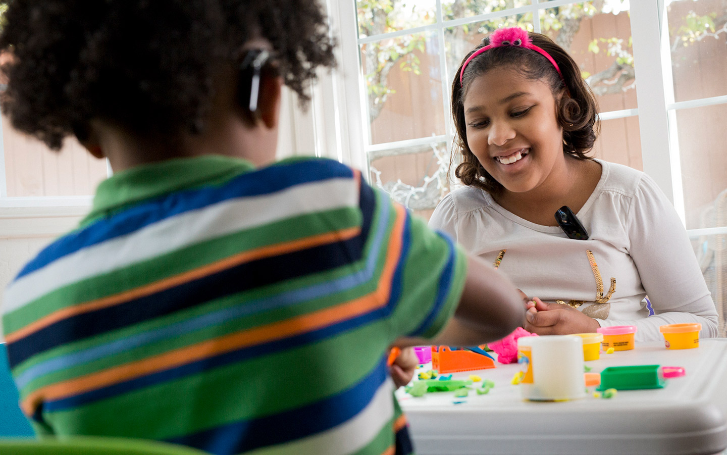 Een meisje draagt een mini-microfoon terwijl ze speelt met een vriendje dat een Cochlear-implantaat draagt