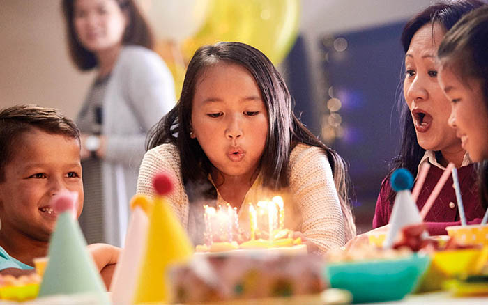 Niña pequeña con implante Cochlear soplando las velas de su pastel de cumpleaños con la familia