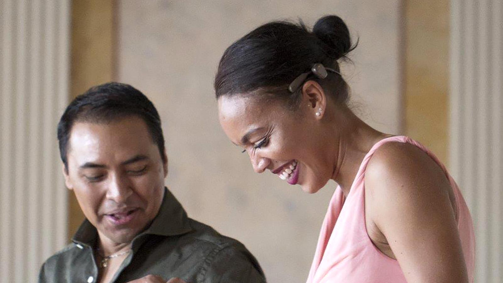 A woman wearing an implant smiles as she holds the hand of a male