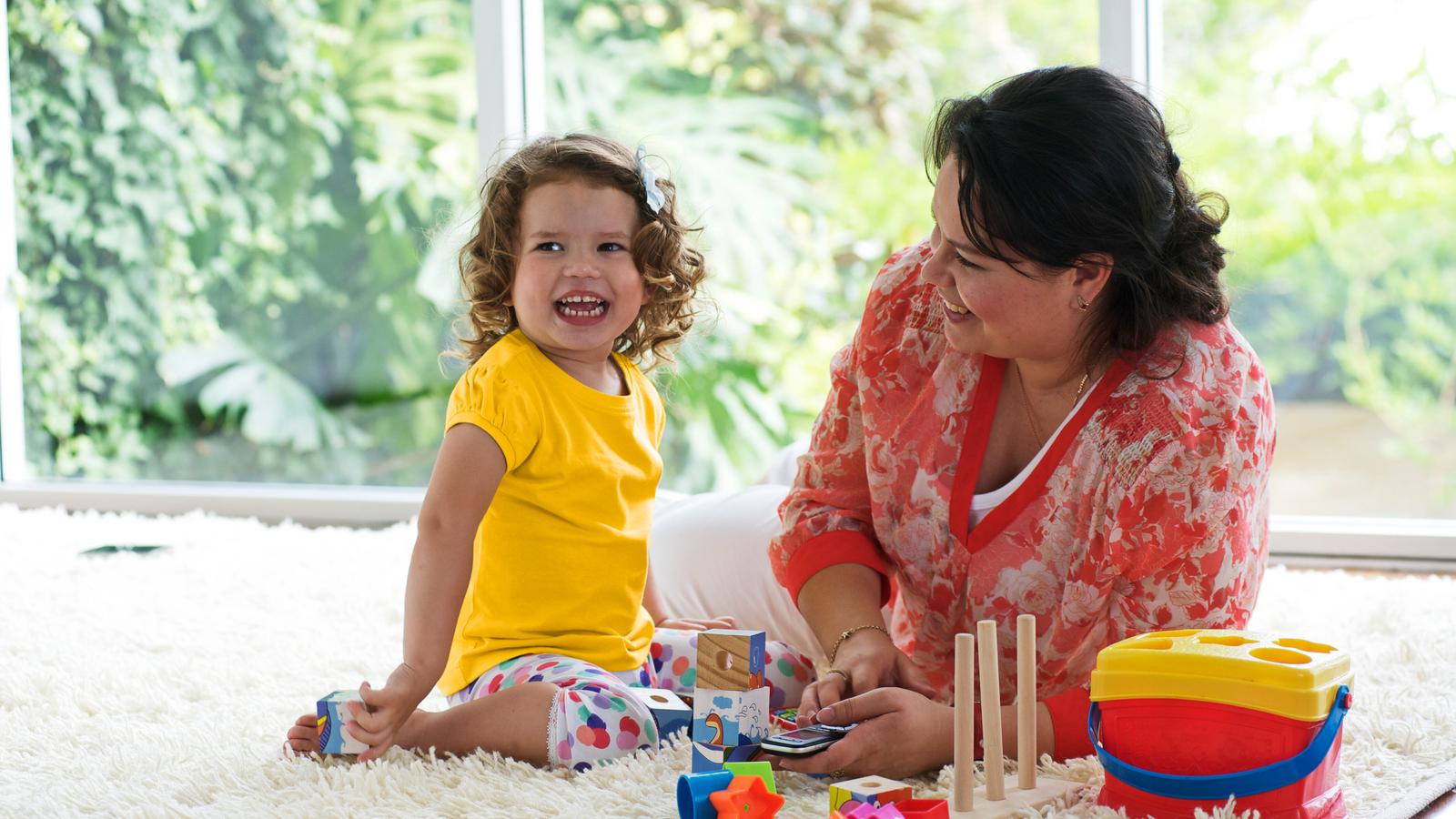 Et lille barn leger på gulvtæppet, mens en kvinde ser på