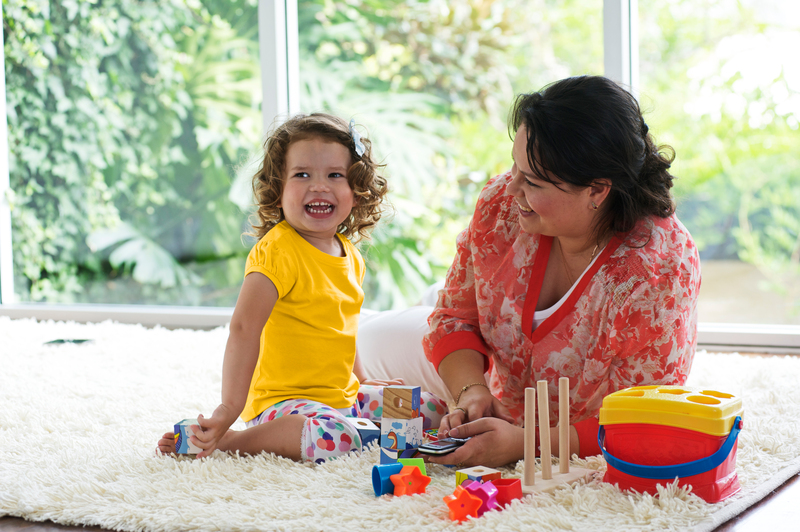 A toddler plays on the carpet as a woman watches on