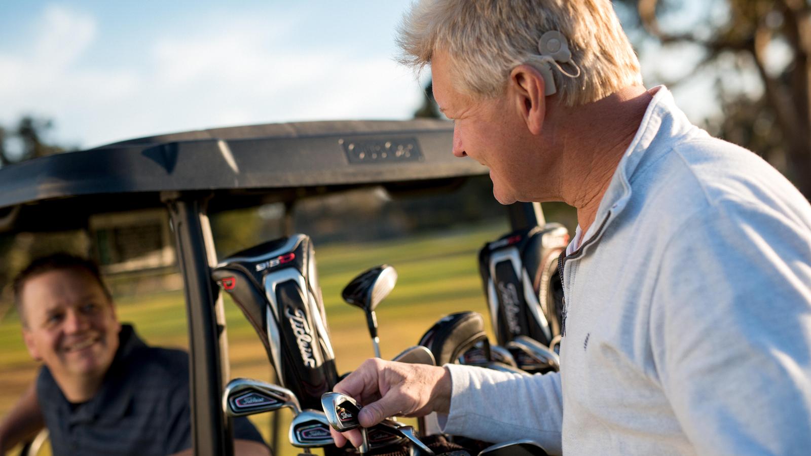 Egy Cochlear implantátumot viselő férfi egy barátjával beszélget a golfpályán.