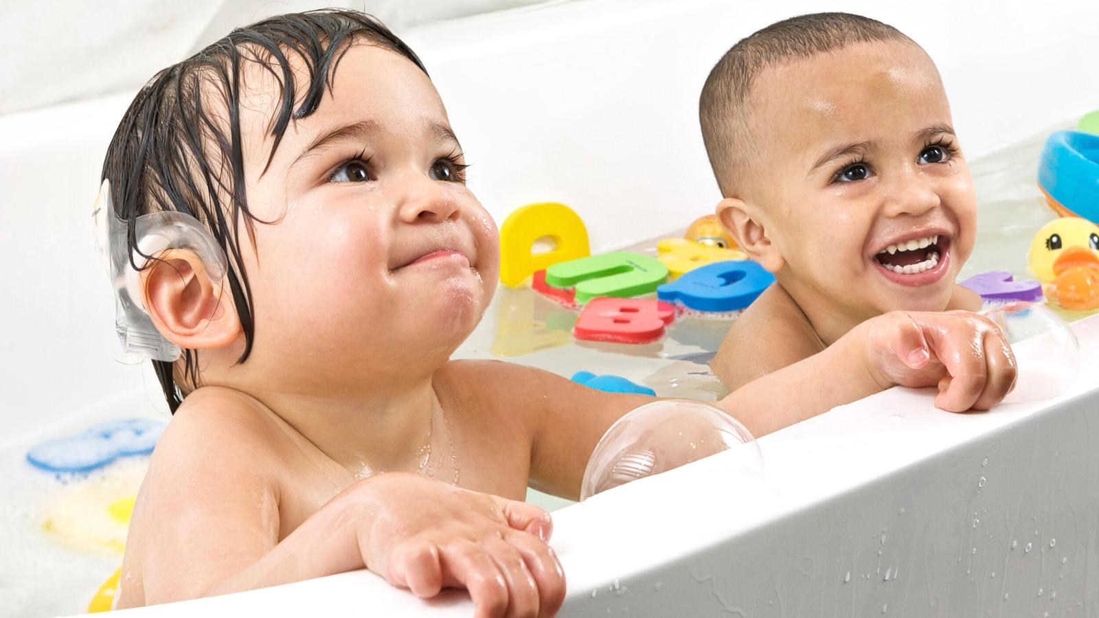 A toddler, one wearing an Aqua Accessory, has a bath with a friend