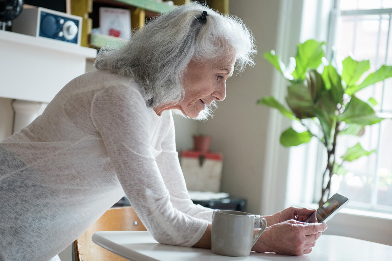 An elderly woman focused on her phone screen, scrolling through content with a look of intrigue.