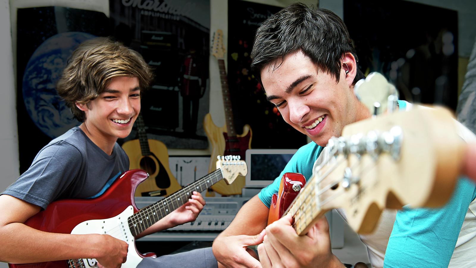 Two teenage males play electric guitar together