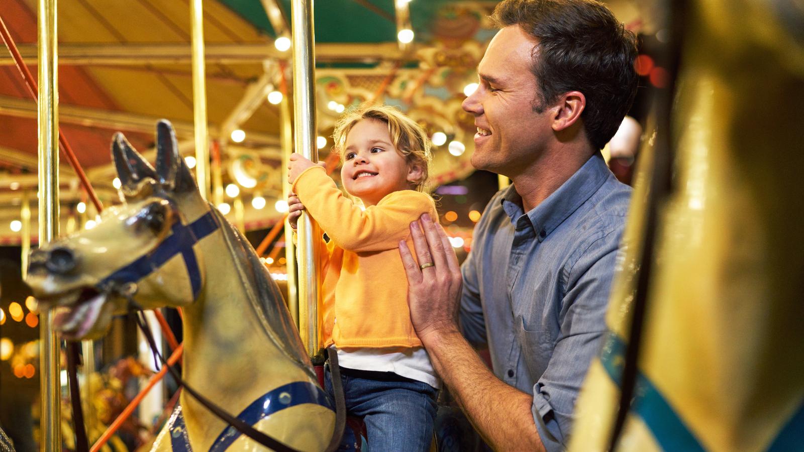 A man holds a child riding on a carousel