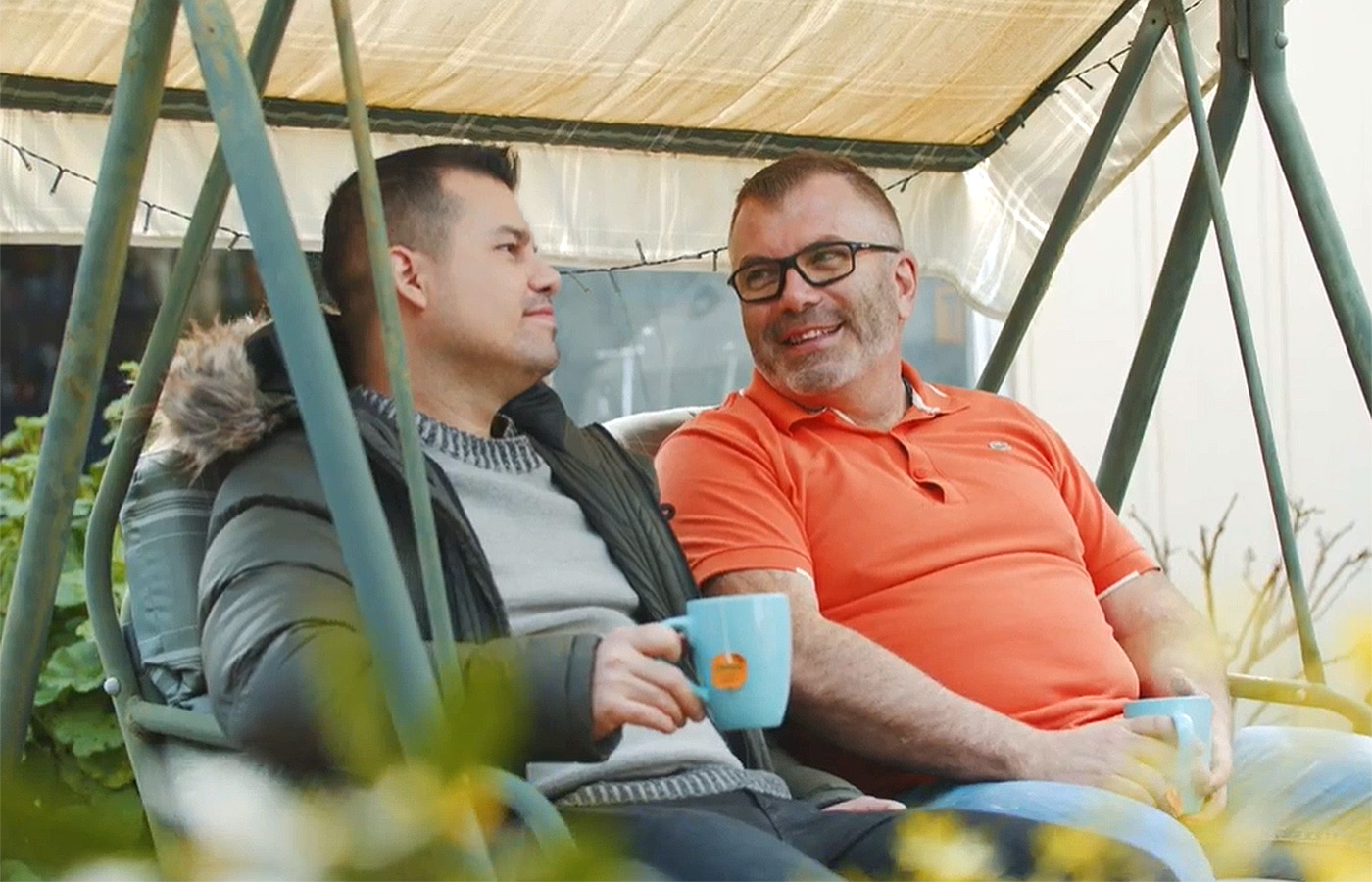 Adrian, porteur de l’implant Osia, et son ami parlent assis sur une balançoire sous le porche